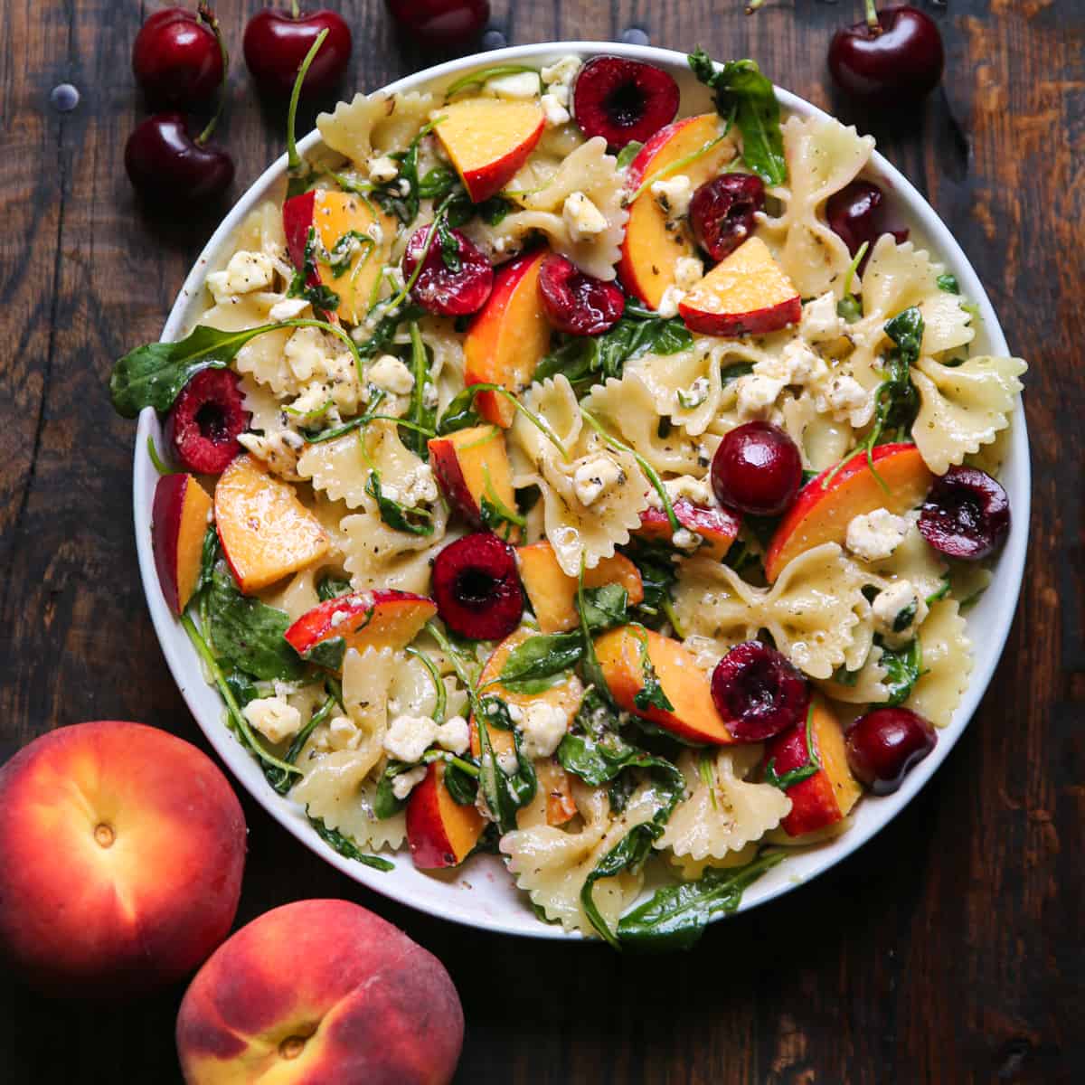 Stone Fruit Salad with Cherries, Peaches, Bow-Tie Pasta, Feta, and Arugula - in a white bowl.