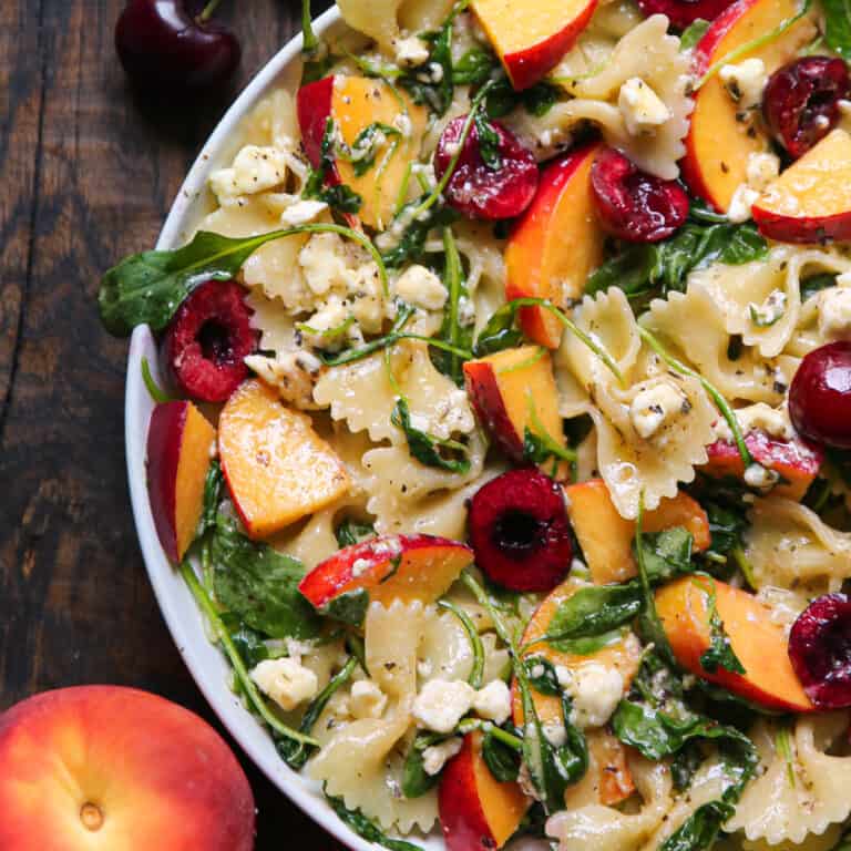 Stone Fruit Salad with Cherries, Peaches, Bow-Tie Pasta, Feta, and Arugula - in a white bowl.