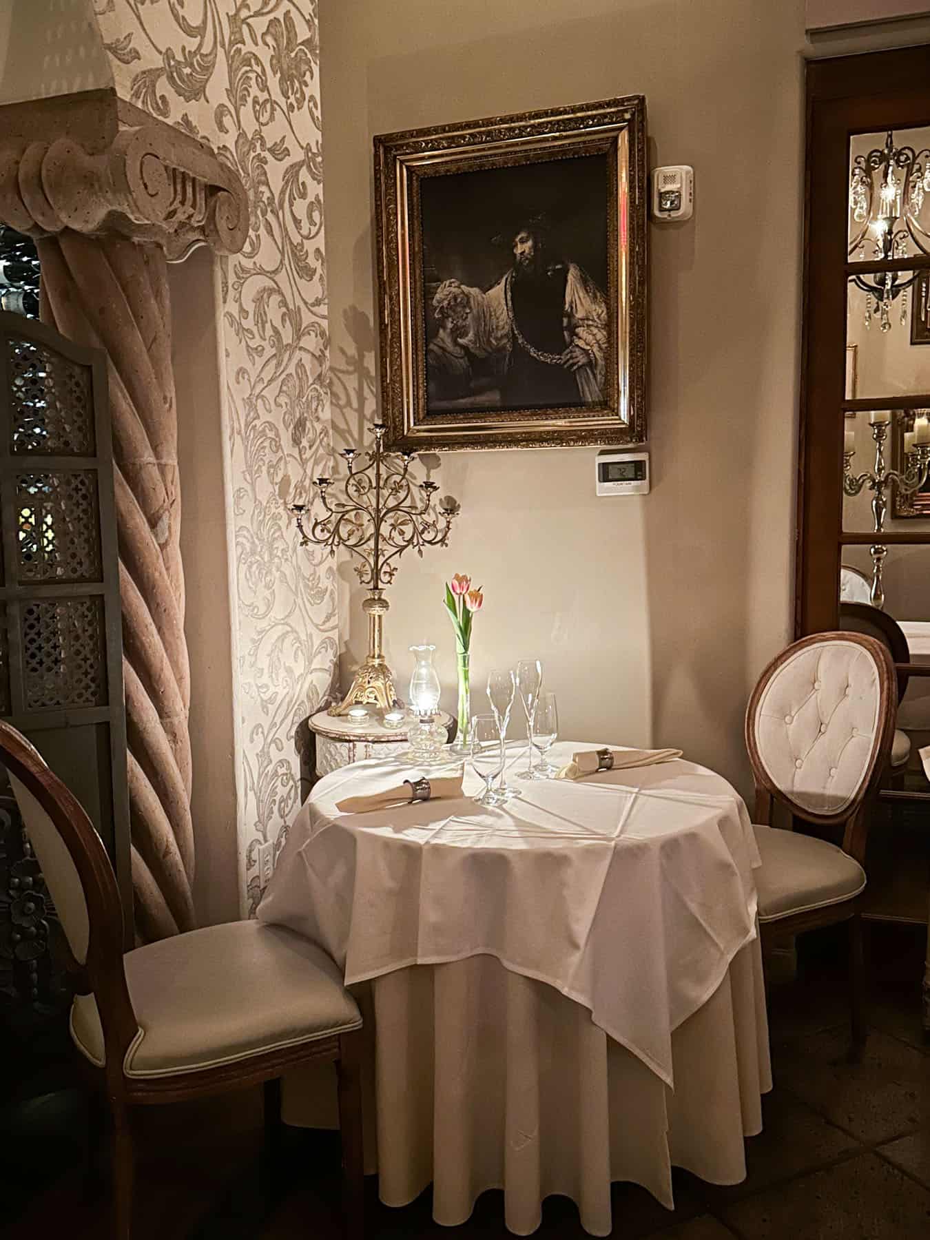 the interior of the restaurant (chairs, dining table with a vase and folded napkins - against the wall with a painting on the wall) at Cafe Monarch in Scottsdale AZ.