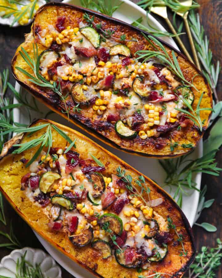 Baked Spaghetti Squash Halves (two) with Zucchini, Corn, Bacon, and Cheese mixture - on a white platter.