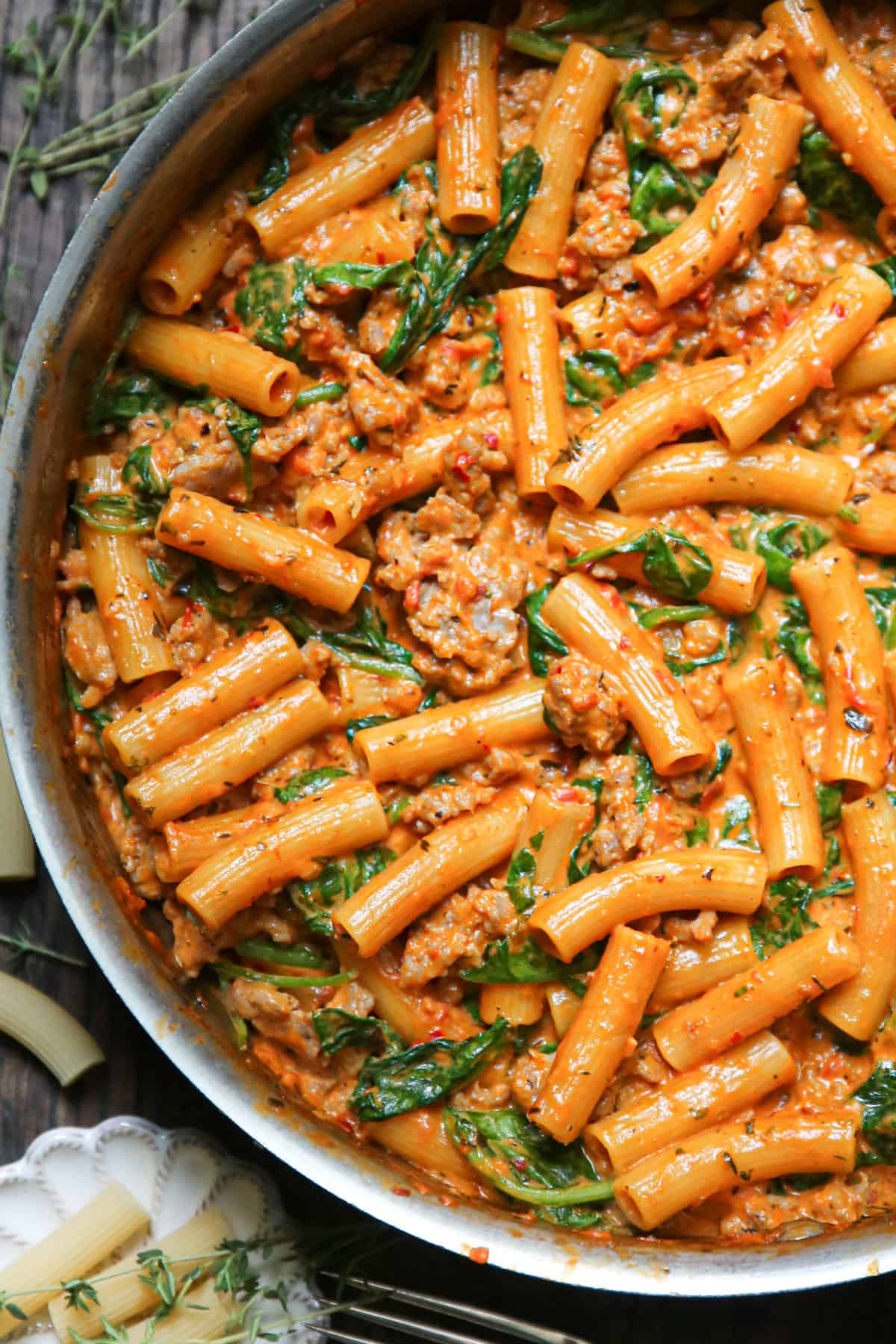 Creamy Sausage Rigatoni with Tomato Sauce and Spinach in a stainless steel pan.