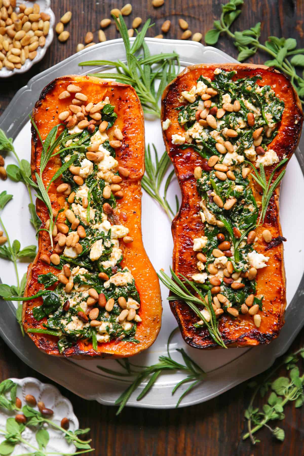 Roasted Butternut Squash Halves (two) stuffed with Feta Cheese and Spinach, topped with pine nuts - on a white platter.