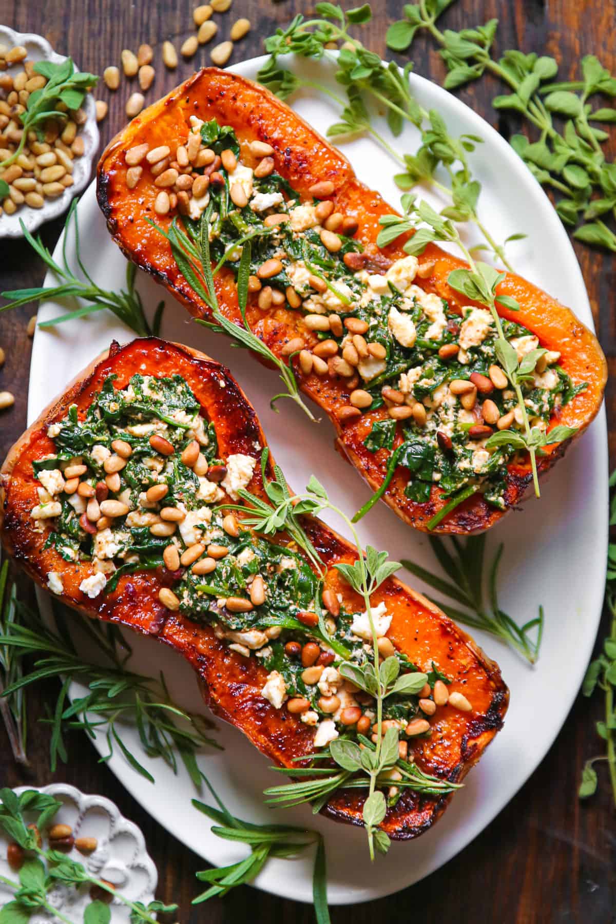 Roasted Butternut Squash Halves (two) stuffed with Feta and Spinach, topped with pine nuts - on a white platter.