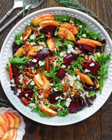 Beet and Apple Salad with Mixed Greens, Pecans, Blue Cheese, and homemade Honey-Lemon Mustard Dressing - in a white bowl.