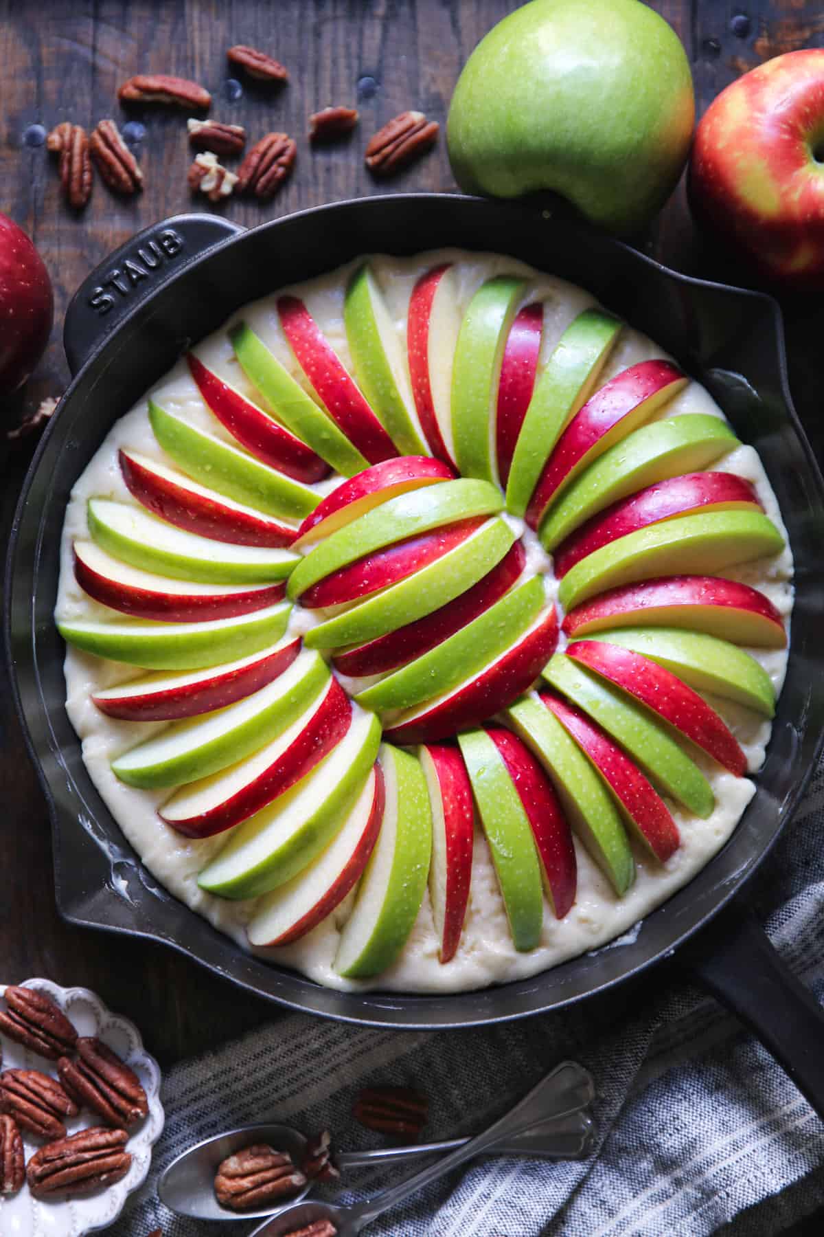 sliced apples on top of cake batter in a cast iron skillet.
