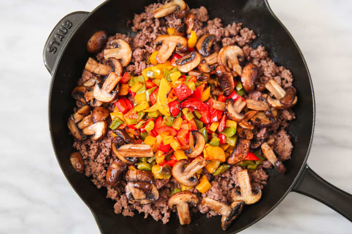 cooked ground beef, bell peppers, mushrooms in a cast iron skillet.