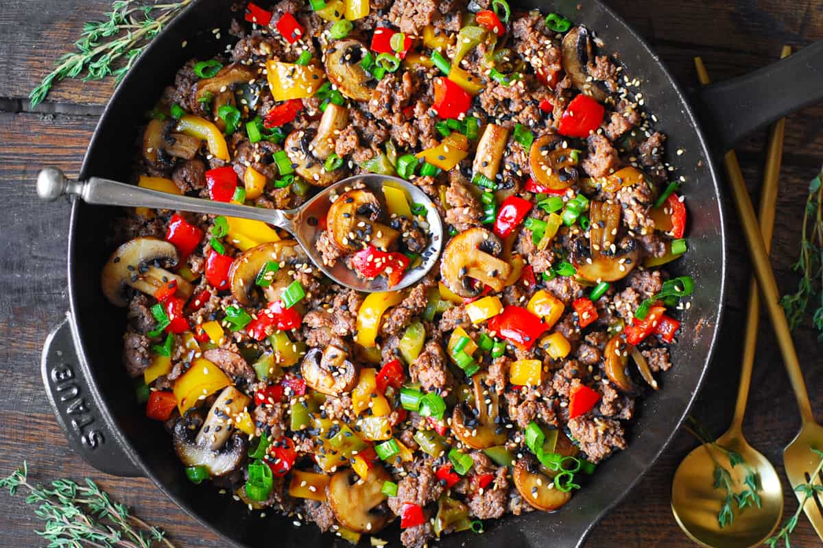 ground beef stir fry with bell peppers and mushrooms in a cast iron skillet.