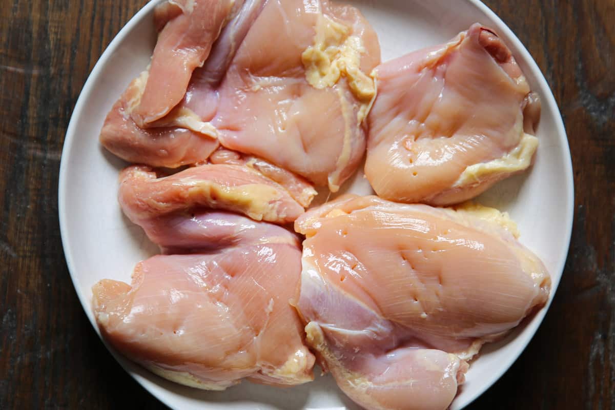 raw chicken thighs on a white plate.