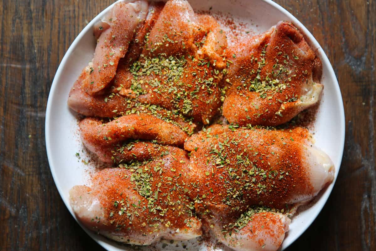 raw chicken thighs with cajun seasoning on a white plate.