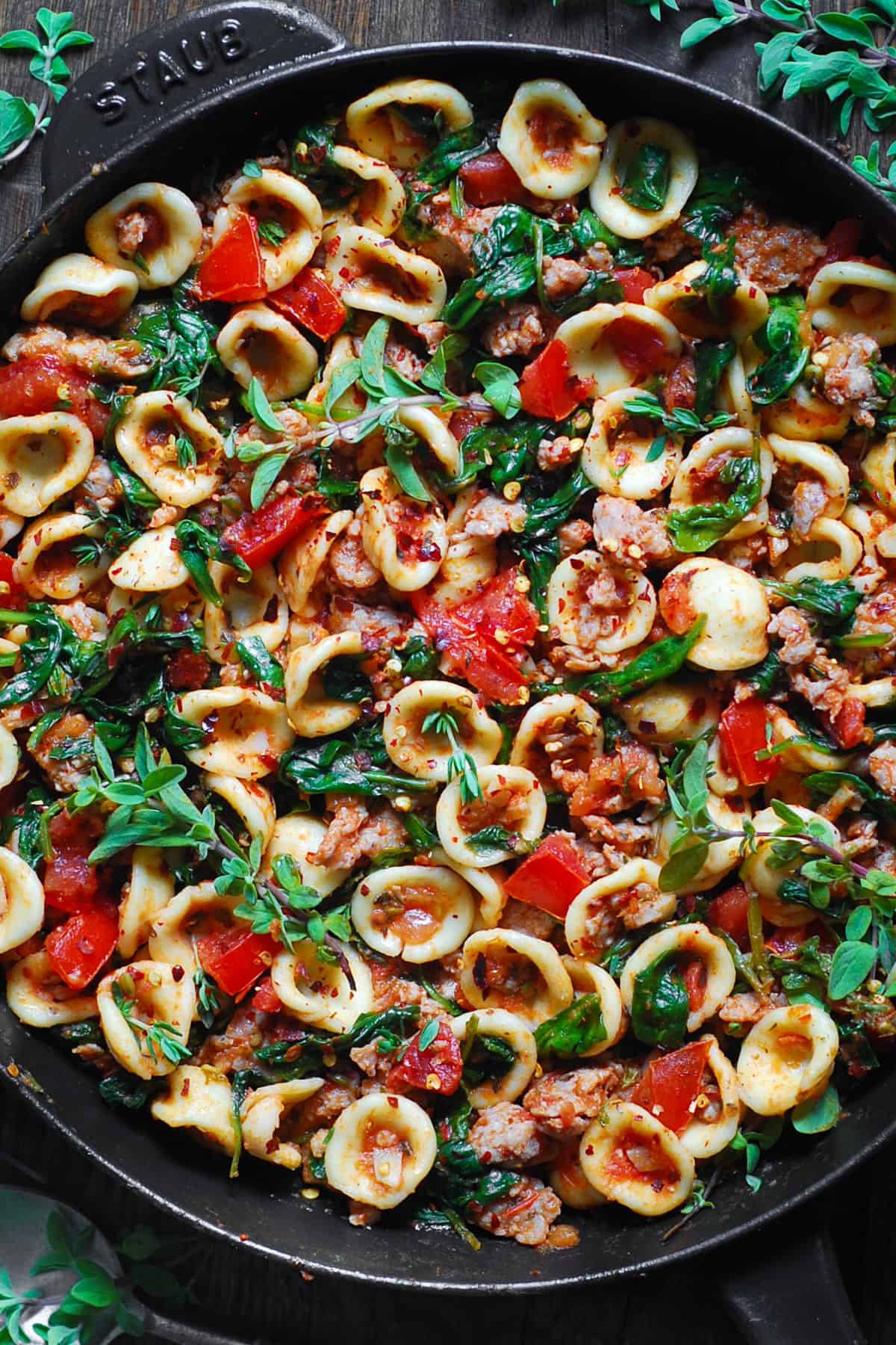 sausage orecchiette with spinach and tomatoes in a cast iron skillet.