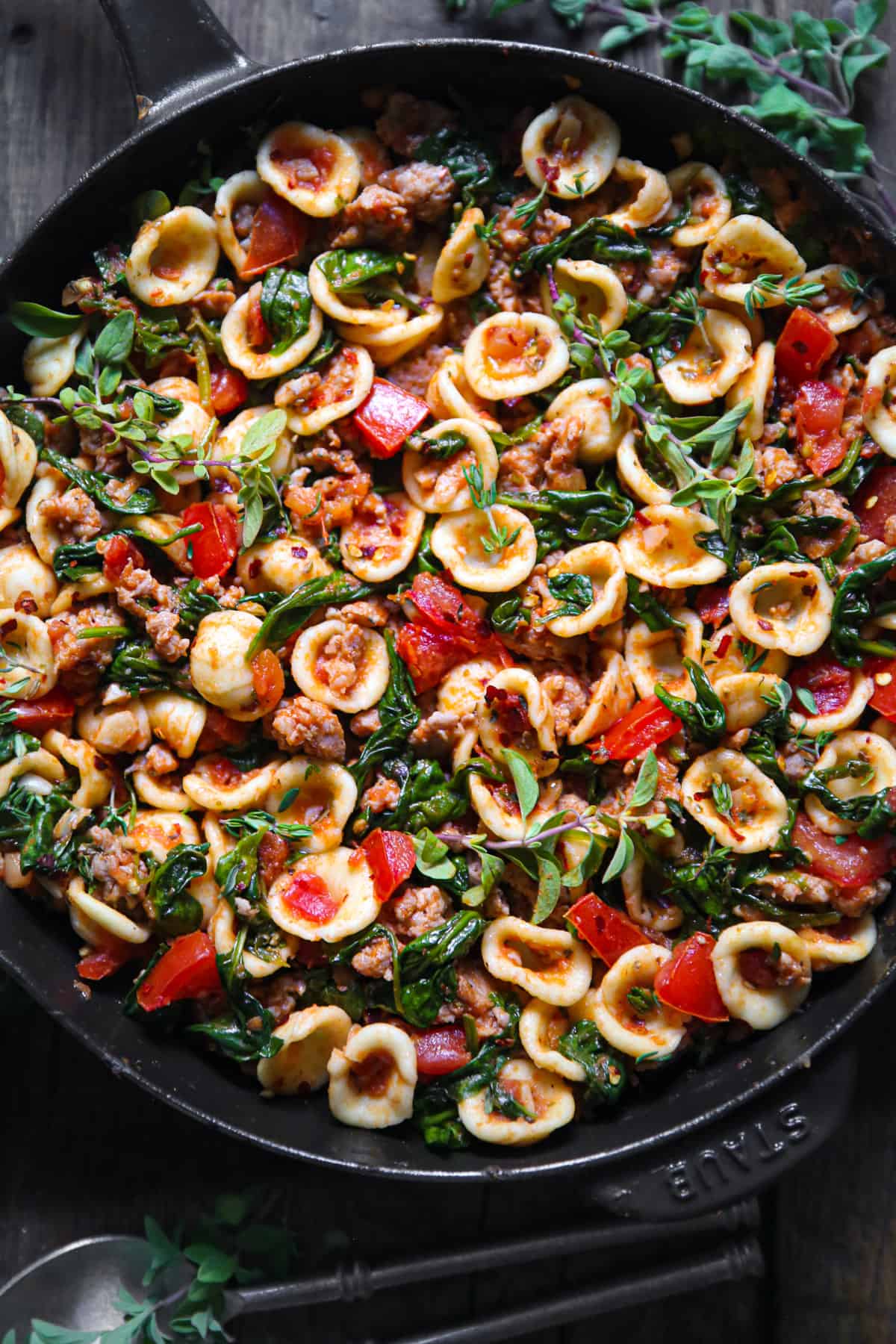 sausage orecchiette with spinach and tomatoes in a cast iron skillet.