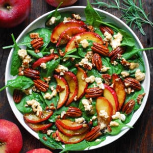 Fall Harvest Salad with Cooked Apples, Pecans, Spinach, Goat Cheese, and Maple-Lime Dressing - in a white bowl.