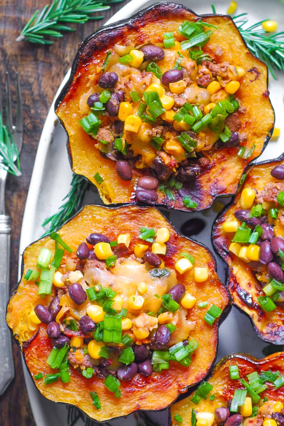 Southwestern Ground Beef Stuffed Acorn Squash with black beans, corn, mild green chiles, and green onions on a white platter.