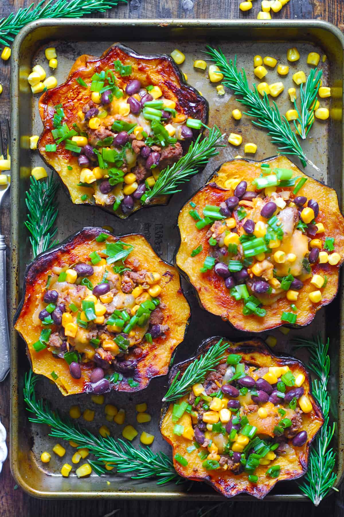 Southwestern Ground Beef Stuffed Acorn Squash with black beans, corn, mild green chiles, and green onions on a baking sheet.