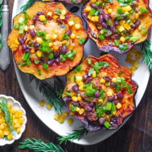 Southwestern Ground Beef Stuffed Acorn Squash with black beans, corn, mild green chiles, and green onions on a white platter.
