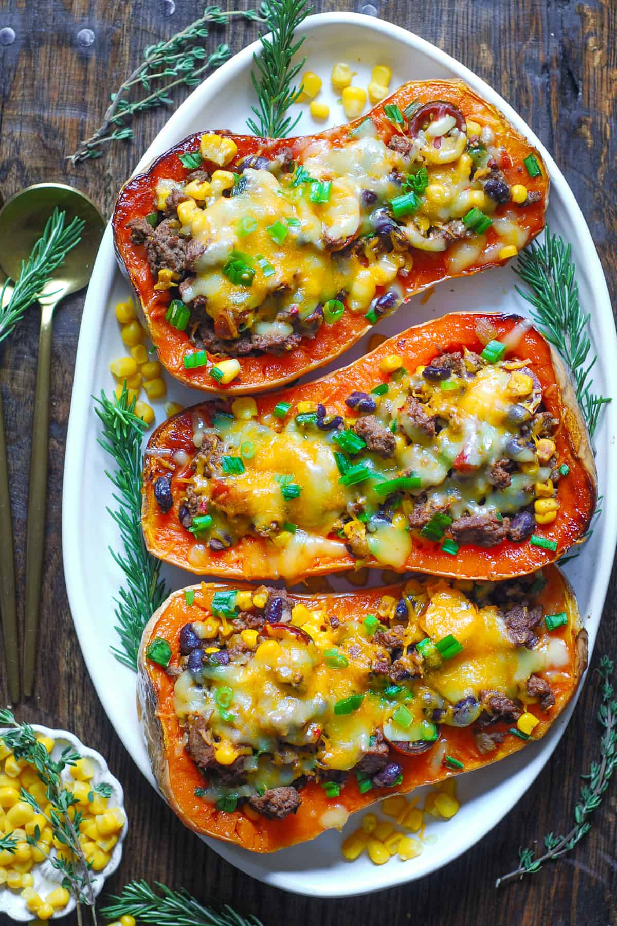 Southwestern Ground Beef Stuffed Butternut Squash with Black Beans, Corn, Tomatoes, Green Onions, mild Green Chiles, Cheddar, and Pepper Jack Cheese on a white platter.
