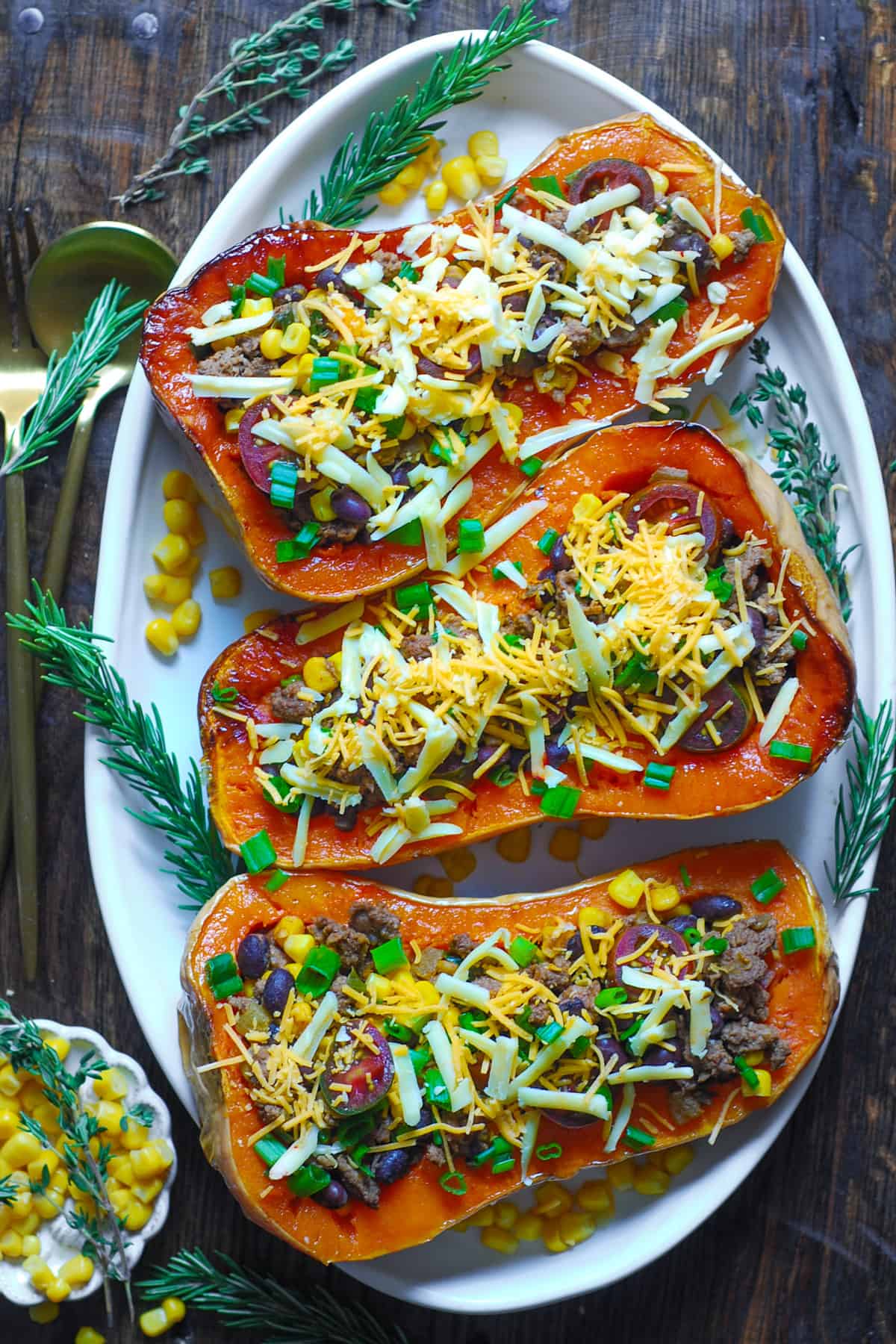 Southwestern Ground Beef Stuffed Butternut Squash with Black Beans, Corn, Tomatoes, Green Onions, mild Green Chiles, Cheddar, and Pepper Jack Cheese on a white platter.
