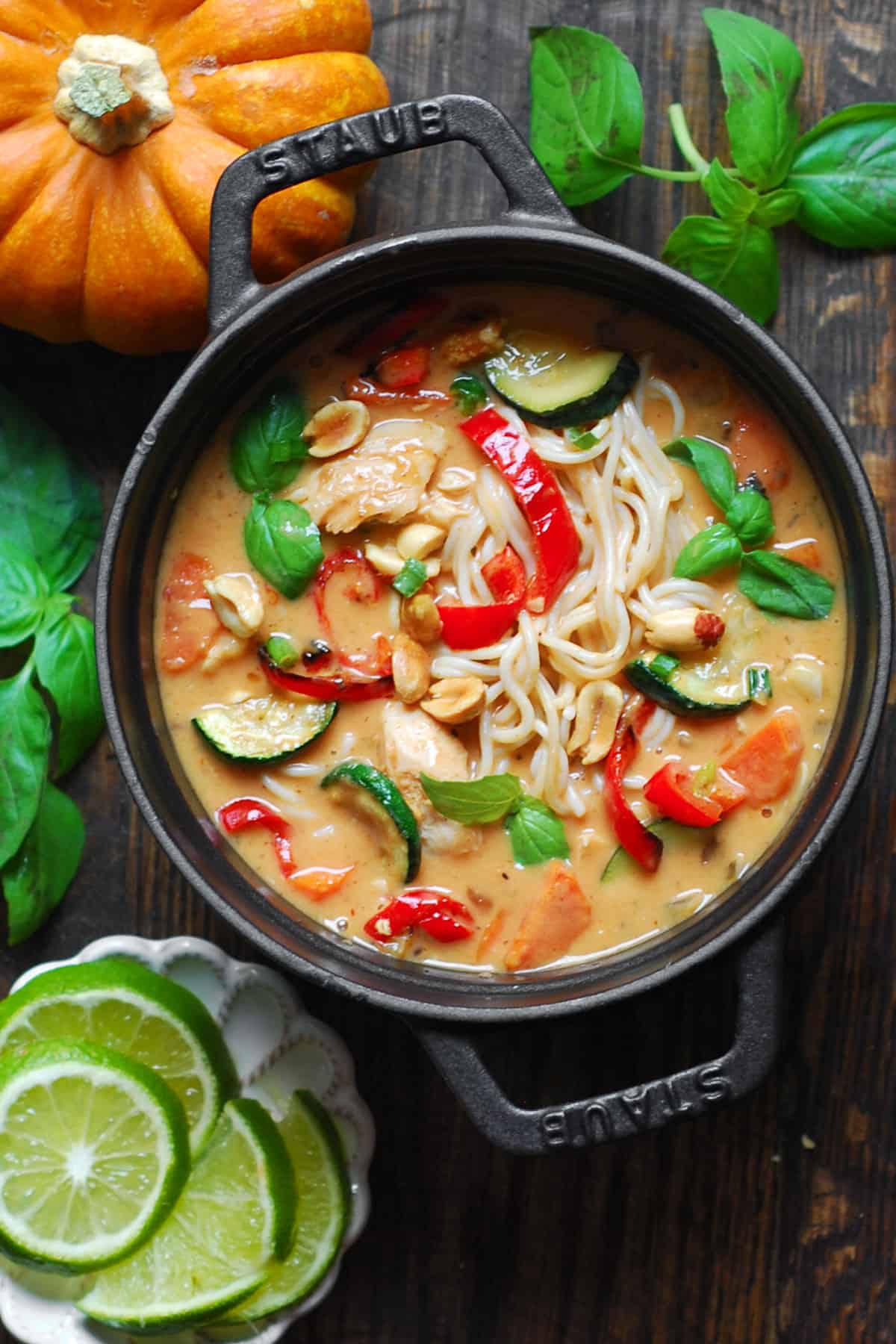 Thai-inspired Red Curry Noodle Soup with chicken, coconut broth, lime juice, red bell peppers, zucchini, carrots, and peanuts - in a small cast iron pan.