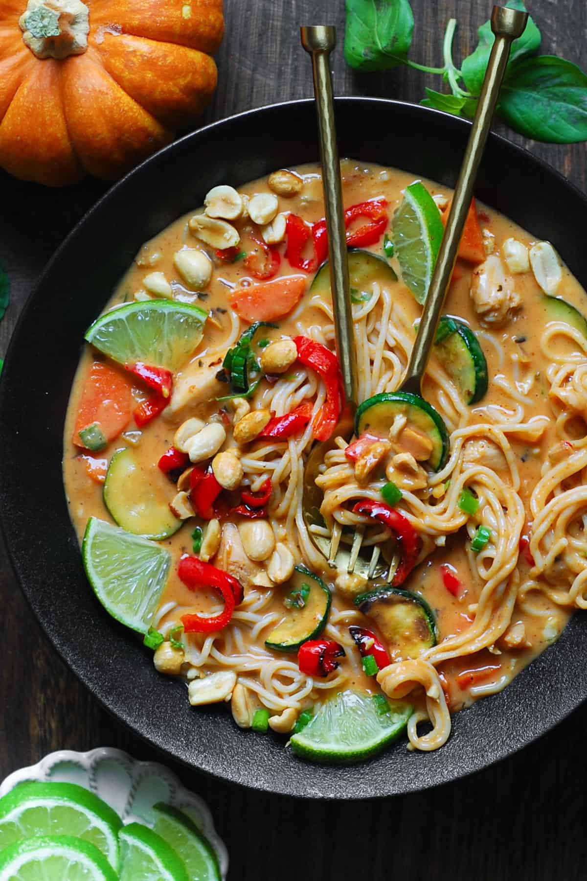 Thai-inspired Red Curry Noodle Soup with chicken, coconut broth, lime juice, red bell peppers, zucchini, carrots, and peanuts - in a black bowl.