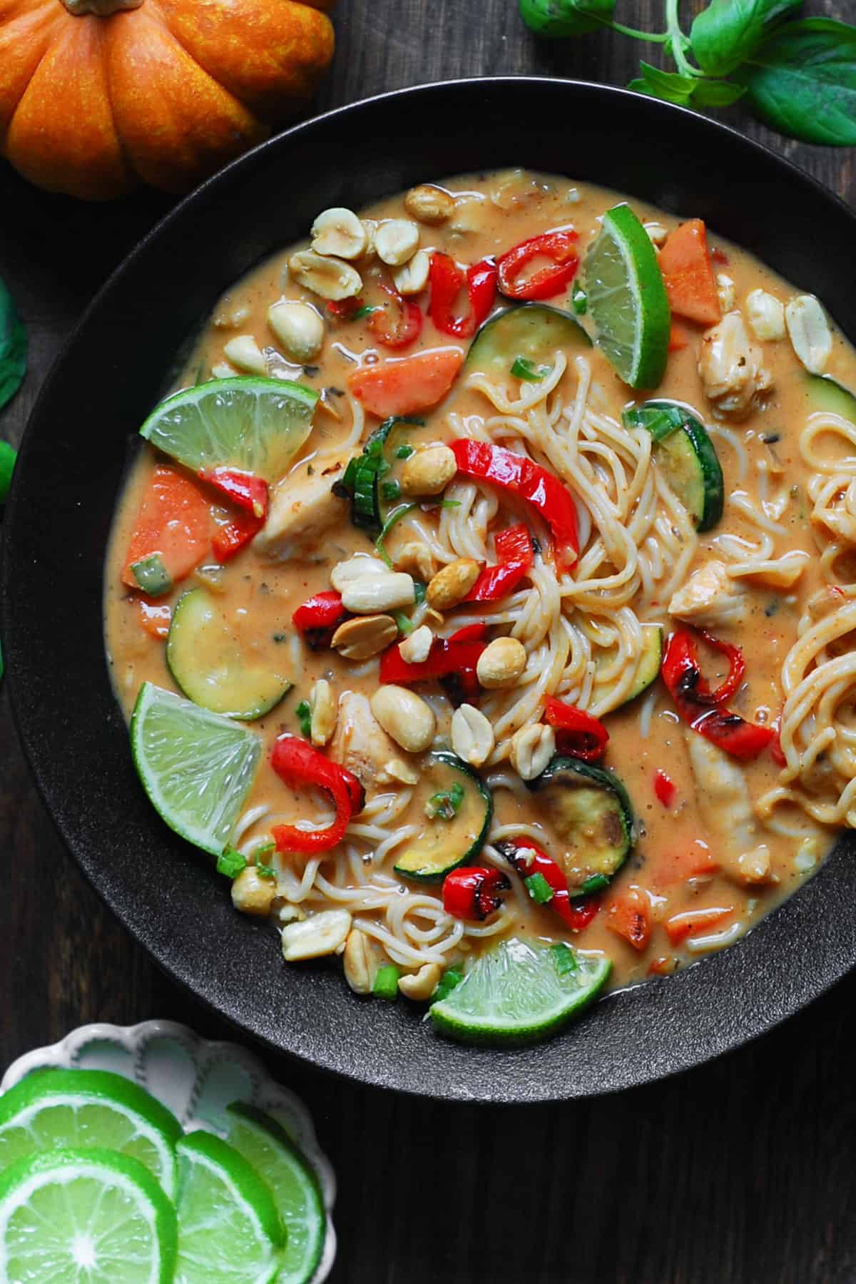 Thai-inspired Red Curry Noodle Soup with chicken, coconut broth, lime juice, red bell peppers, zucchini, carrots, and peanuts - in a black bowl.