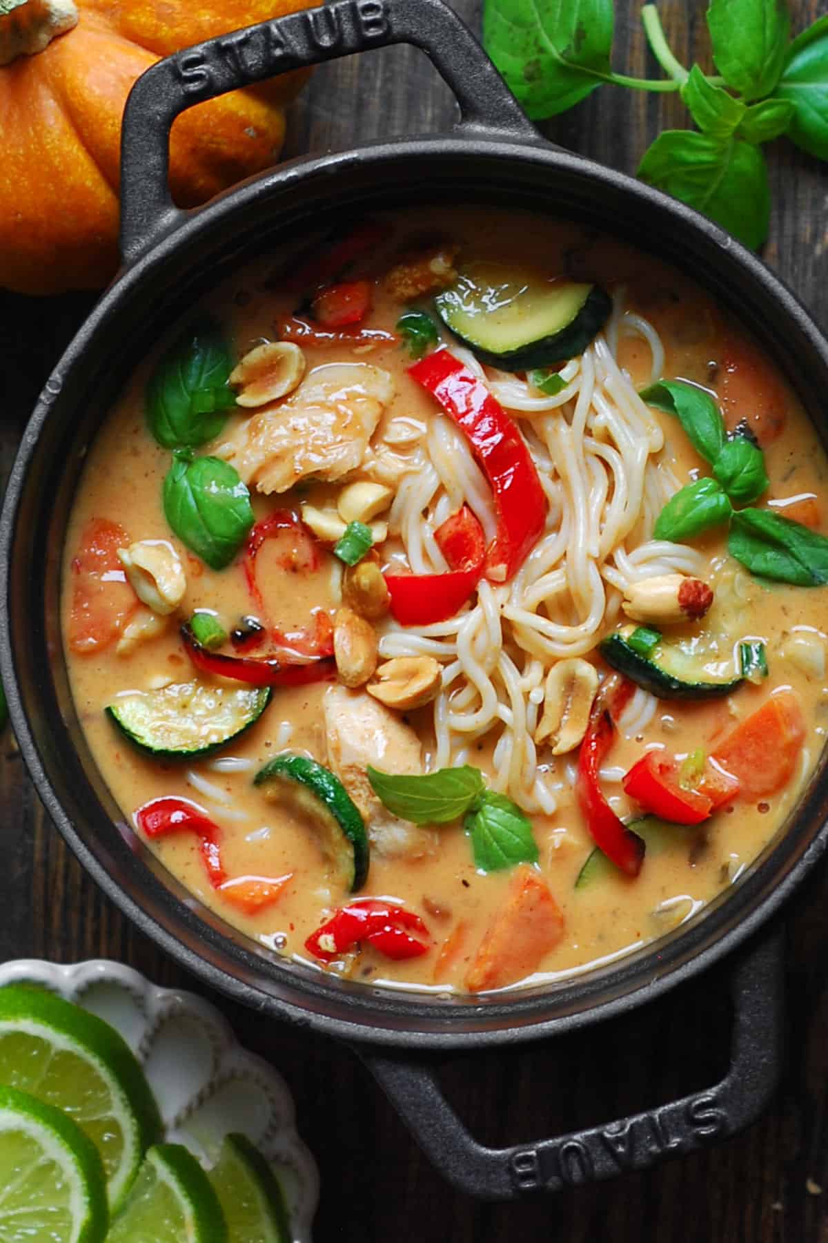 Thai-inspired Red Curry Noodle Soup with chicken, coconut broth, lime juice, red bell peppers, zucchini, carrots, and peanuts - in a cast iron soup pan.