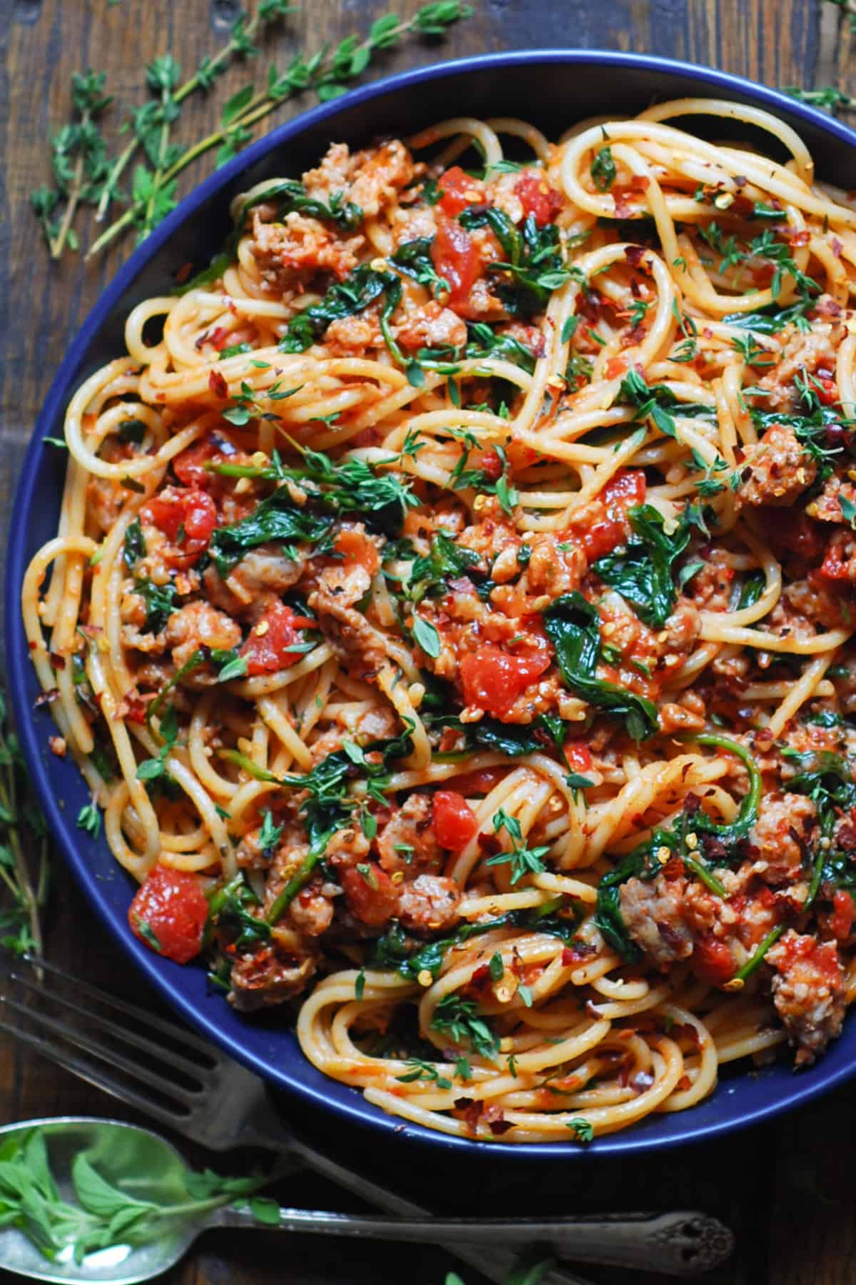 Italian Sausage Spaghetti with Spinach and Tomatoes in a blue bowl.