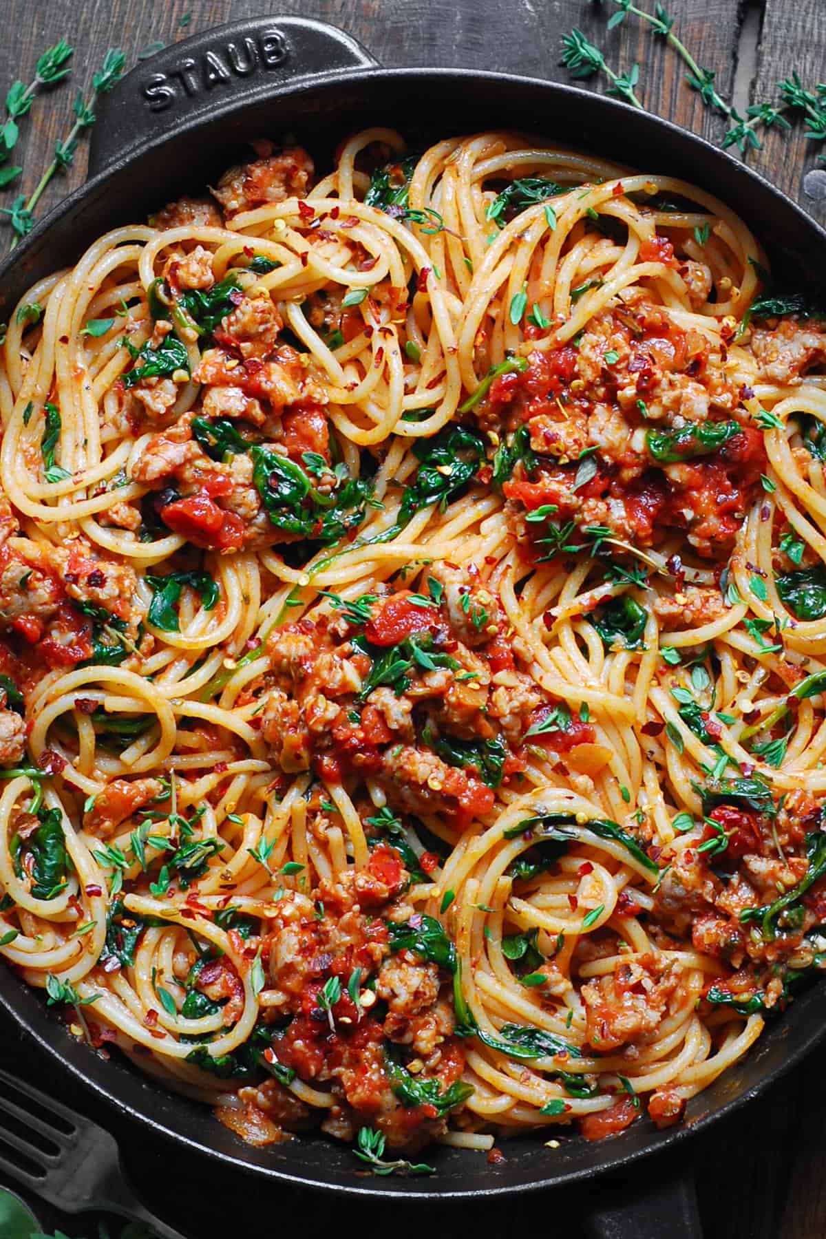 Italian Sausage Spaghetti with Spinach and Tomatoes in a cast iron pan.