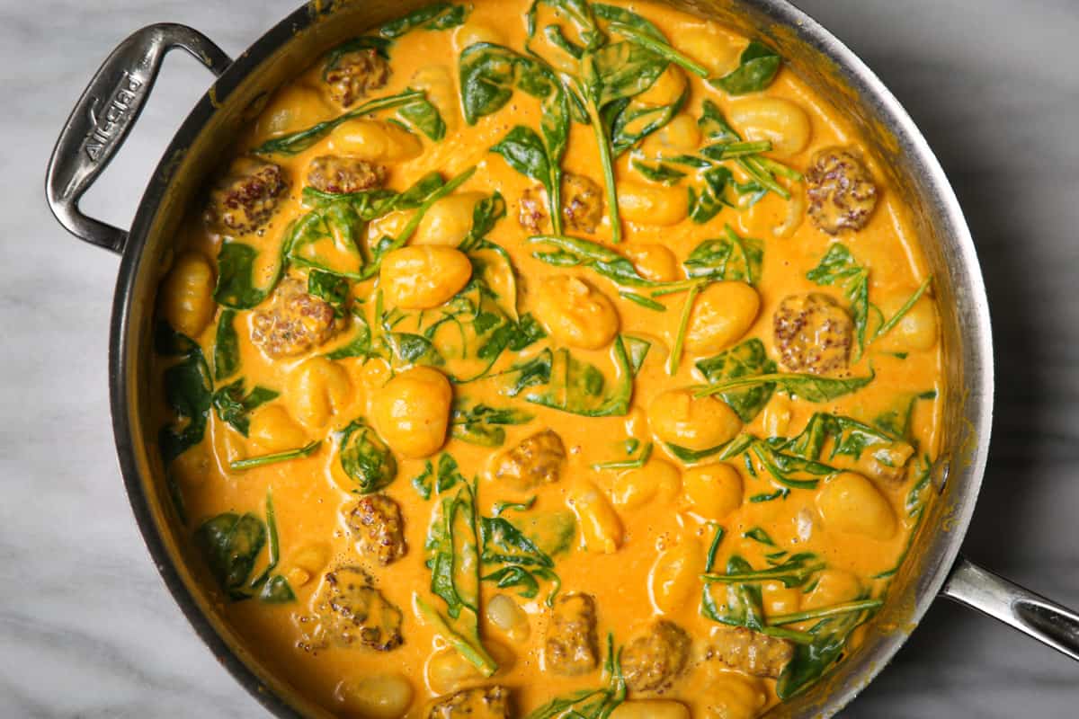 creamy pumpkin gnocchi with sausage and spinach in a stainless steel pan.