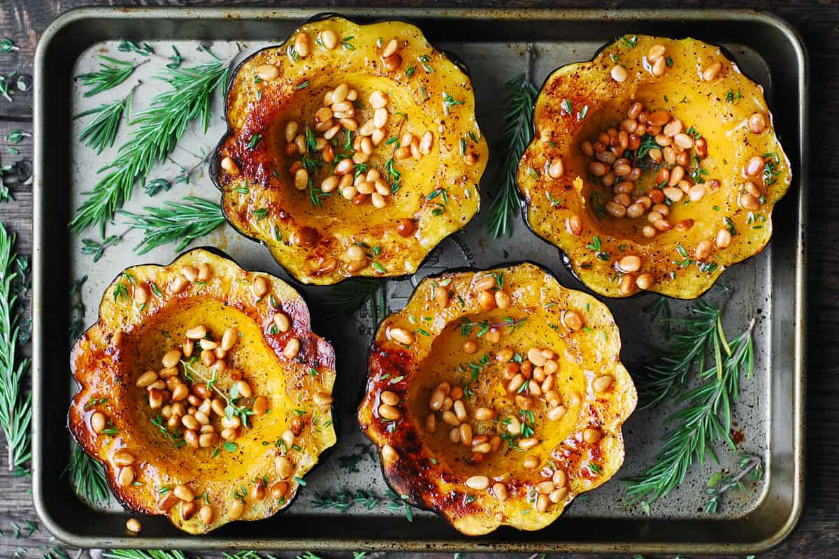 four roasted acorn squash halves with toasted pine nuts and fresh thyme on a baking sheet.