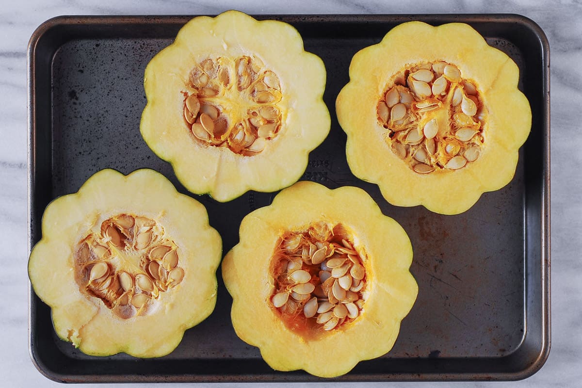 two acorn squashes cut in half with seeds on a baking sheet.