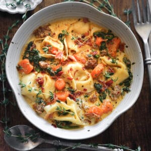 Creamy Italian Sausage Tortellini Soup with Spinach and Carrots in a white bowl.