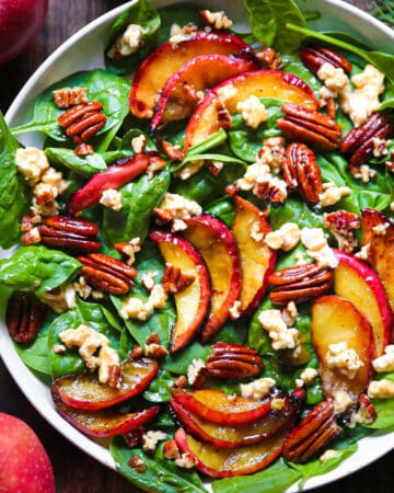 Spinach Salad with Cooked Apples, Pecans, and Goat Cheese - in a white bowl.