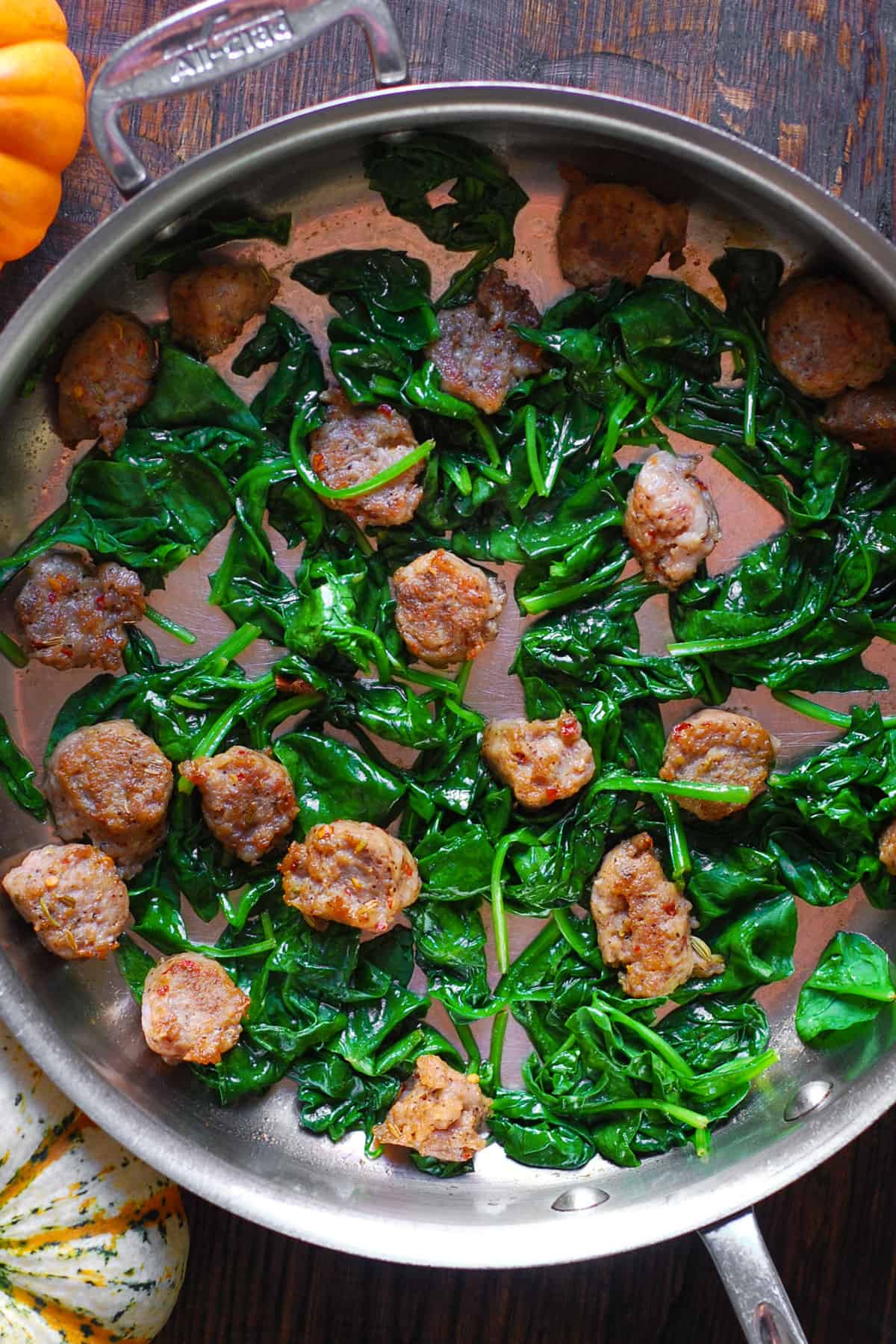 Cooked sliced sausage and cooked spinach - in a stainless steel pan.