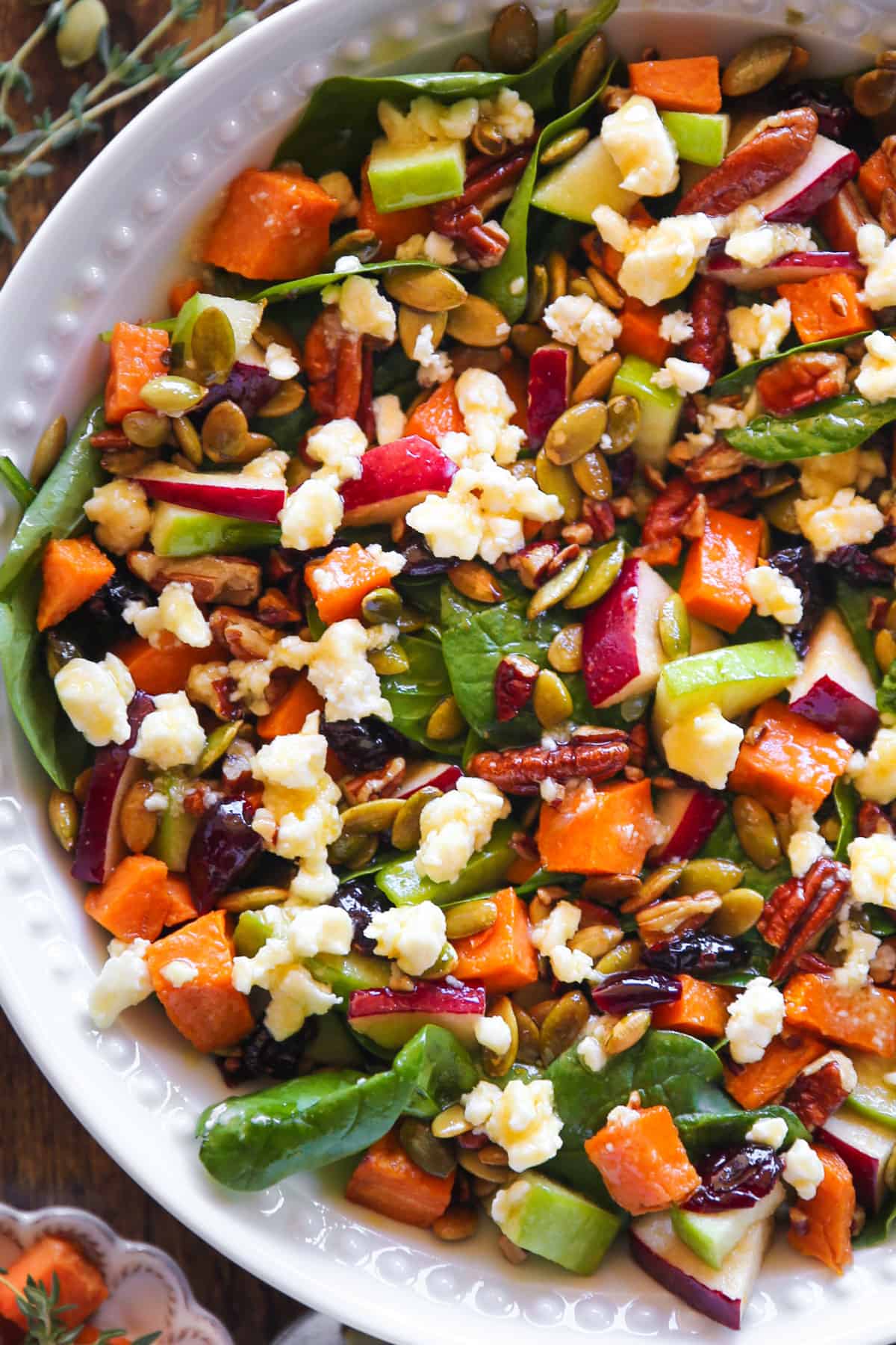 Roasted Sweet Potato Salad with spinach, apples, dried cranberries, pecans, pumpkin seeds, and feta cheese - in a white bowl.