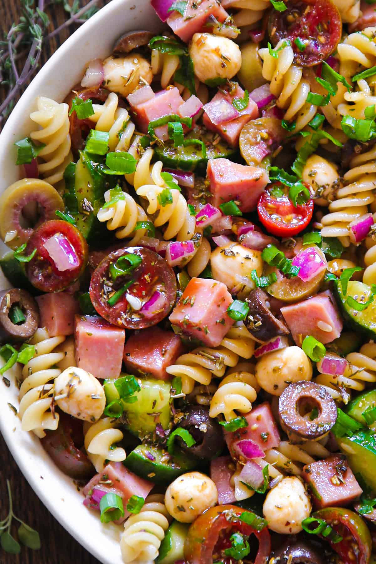 Ham Pasta Salad with Tomatoes, Cucumbers, Red Onions, Green Onions, Olives, Mozzarella Cheese in a white bowl.
