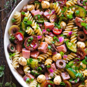 Ham Pasta Salad with Tomatoes, Cucumbers, Red Onions, Green Onions, Olives, Mozzarella Cheese in a white bowl.