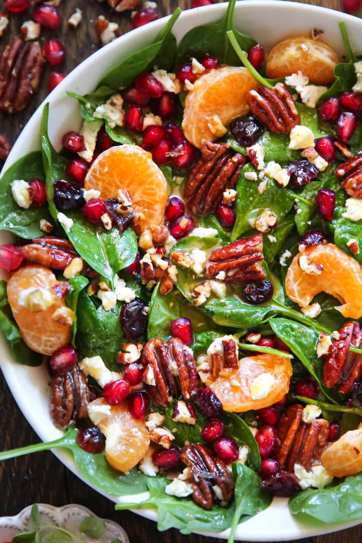 Christmas Salad with Spinach, Pecans, Mandarin Oranges, Pomegranate Arils in a white bowl.