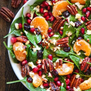 Christmas Salad with Spinach, Pecans, Mandarin Oranges, Pomegranate Arils in a white bowl.