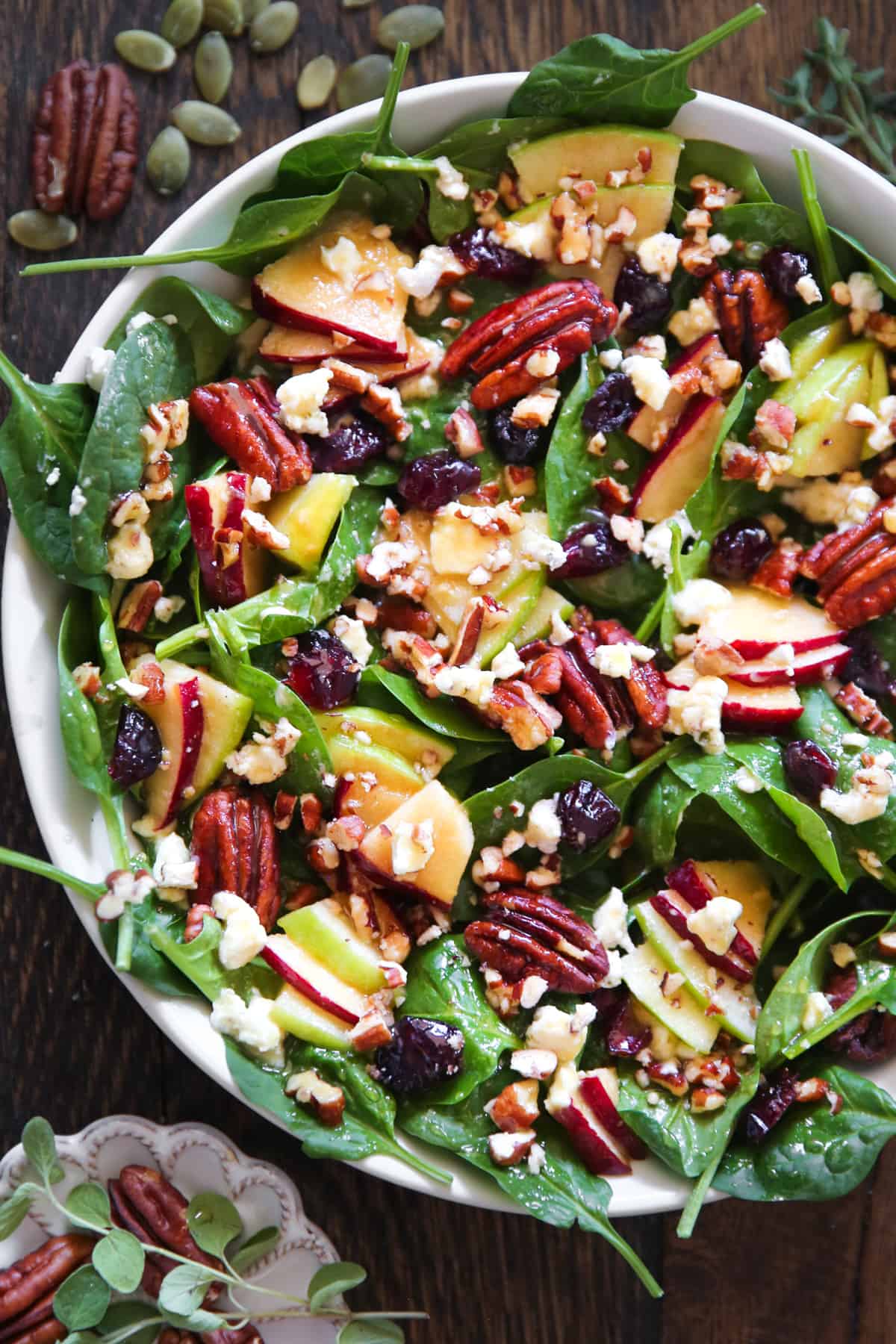 Apple Spinach Salad with Cranberries, Pecans, and Goat Cheese in a white bowl.