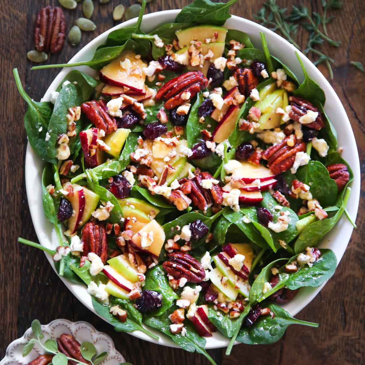 Apple Spinach Salad with Cranberries, Pecans, and Goat Cheese in a white bowl.