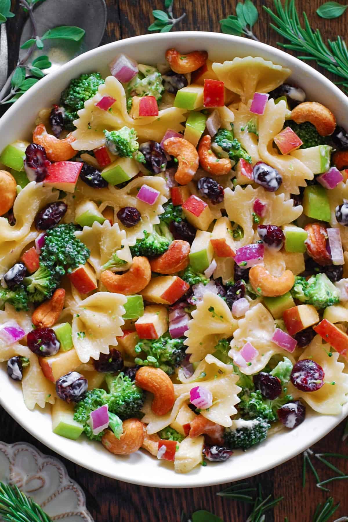 Broccoli Pasta Salad with Cranberries, Apples, Cashews, and Red Onions in a white bowl.