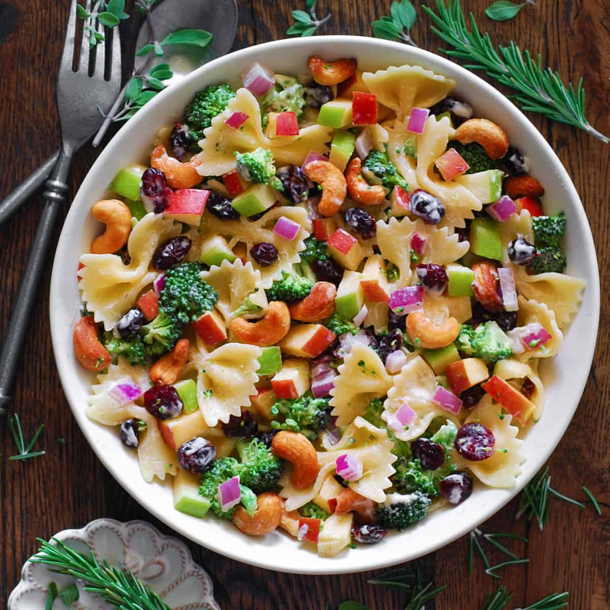 Broccoli Pasta Salad with Cranberries, Apples, Cashews, and Red Onions in a white bowl.