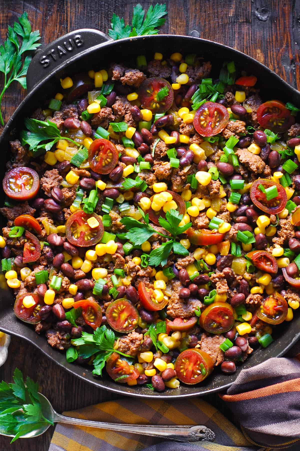 Mexican Ground Beef with tomatoes, black beans, corn, mild green chiles, and green onions in a cast iron skillet.