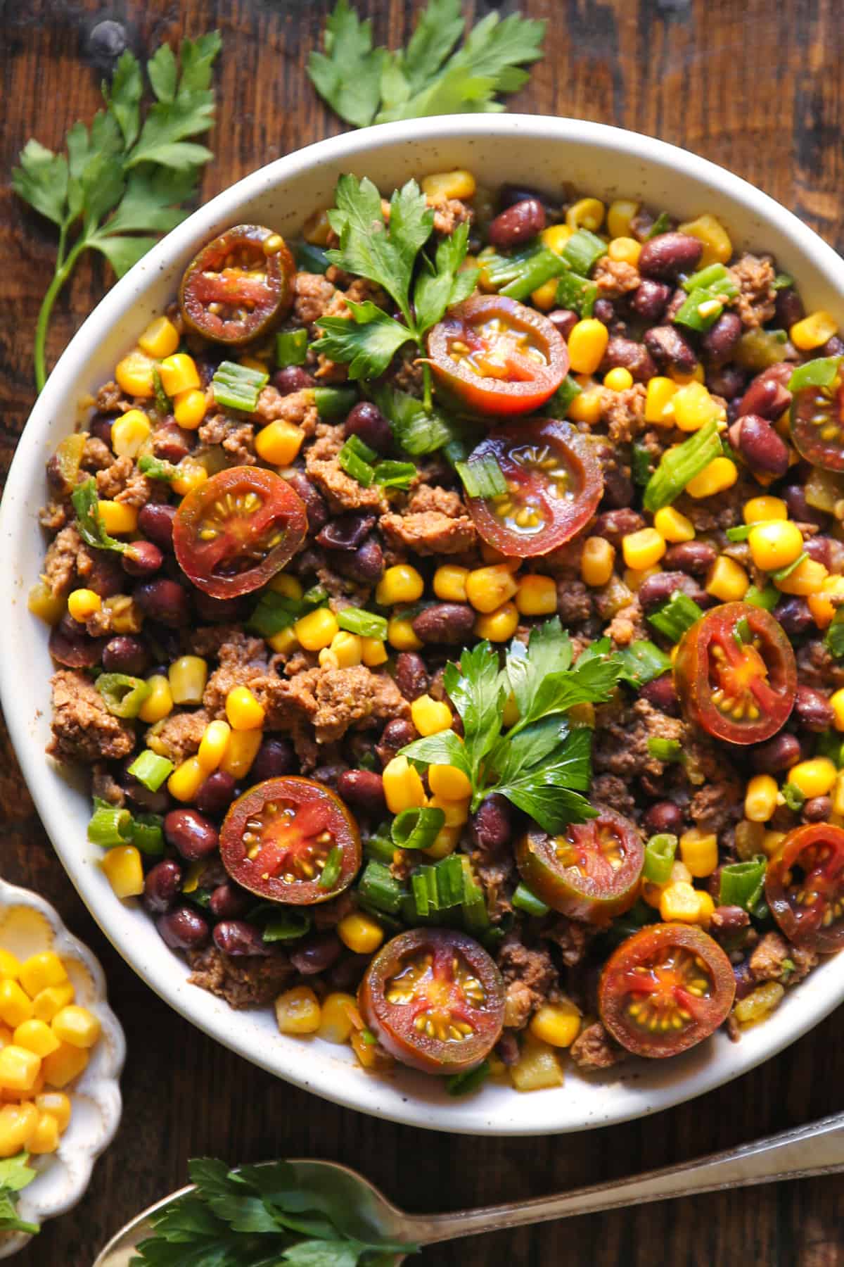 Mexican Ground Beef with tomatoes, black beans, corn, mild green chiles, and green onions in a white bowl.