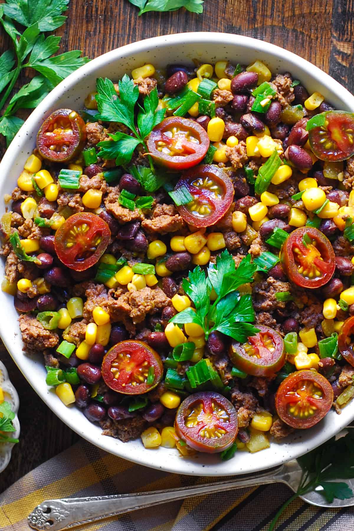 Mexican Ground Beef with tomatoes, black beans, corn, mild green chiles, and green onions in a white bowl.