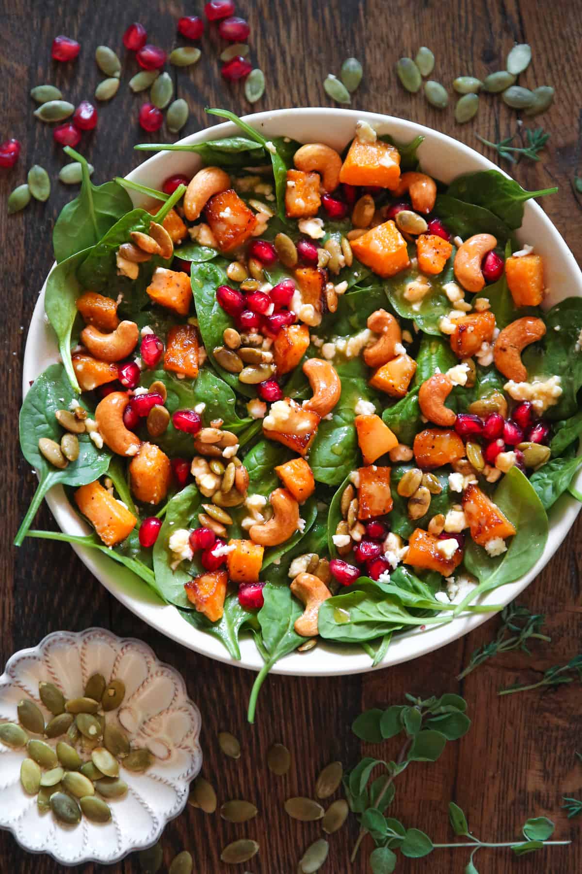 Butternut squash salad with spinach, cashews, pumpkin seeds, feta cheese, pomegranate seeds, and mustard honey-lime dressing in a white bowl.
