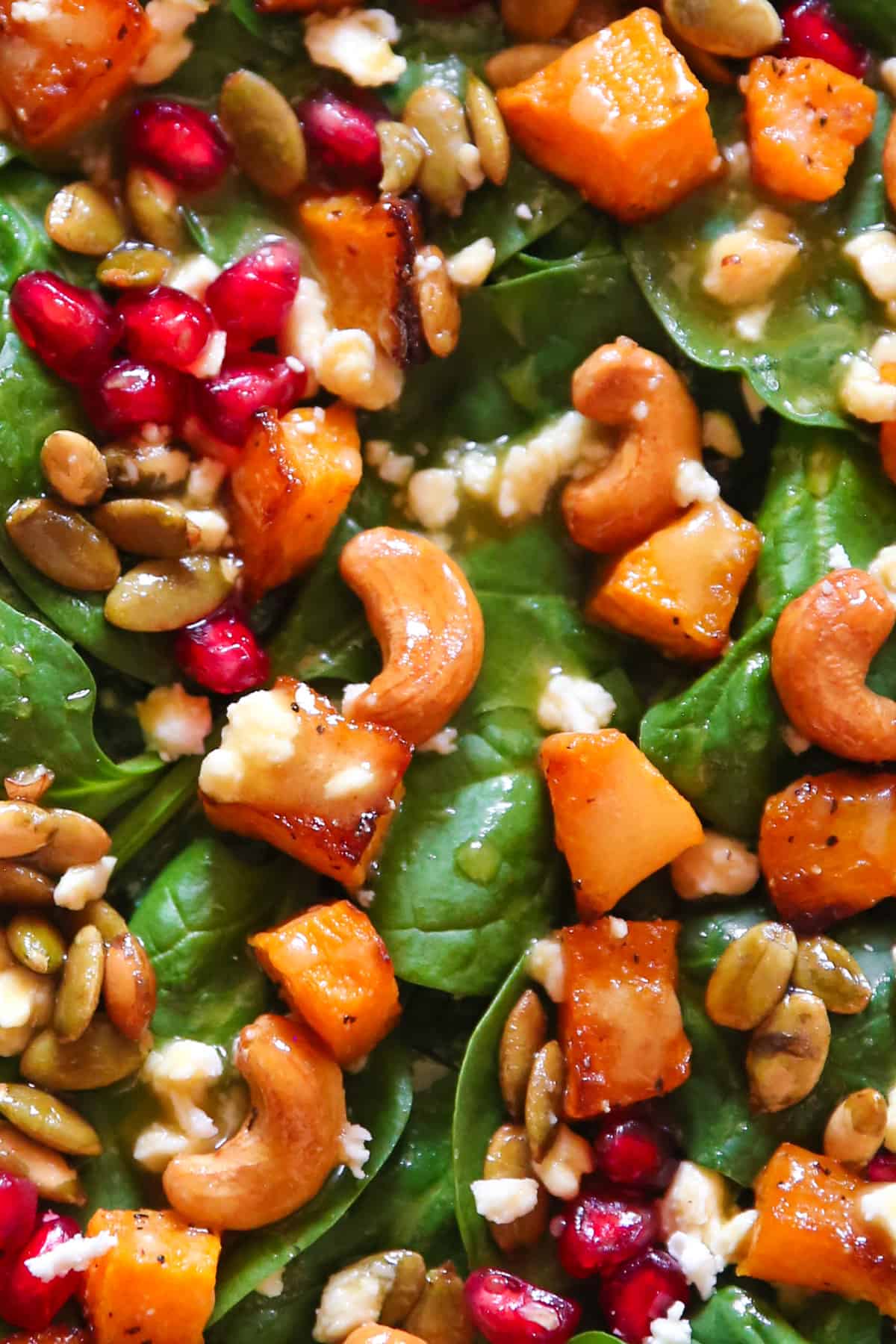 Butternut squash salad with spinach, cashews, pumpkin seeds, feta cheese, pomegranate seeds, and mustard honey-lime dressing - close-up photo.