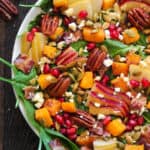 Fall Harvest Salad with Spinach, Butternut Squash, Apple, Pear, Pecans, Pumpkin Seeds, Bacon, Feta Cheese, Pomegranate Arils in a white bowl.