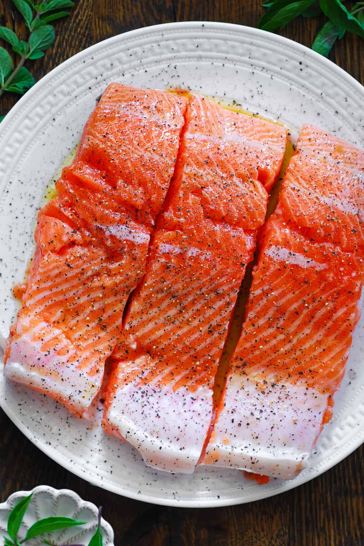 3 raw salmon fillets on a white plate.