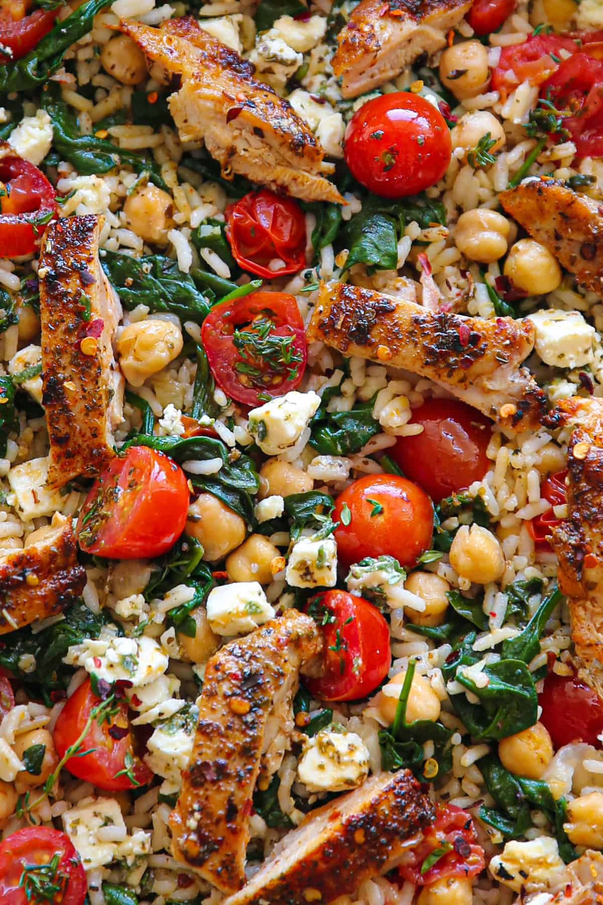 Greek Chicken and Lemon Rice with spinach, grape tomatoes, chickpeas, and feta cheese (close-up photo).